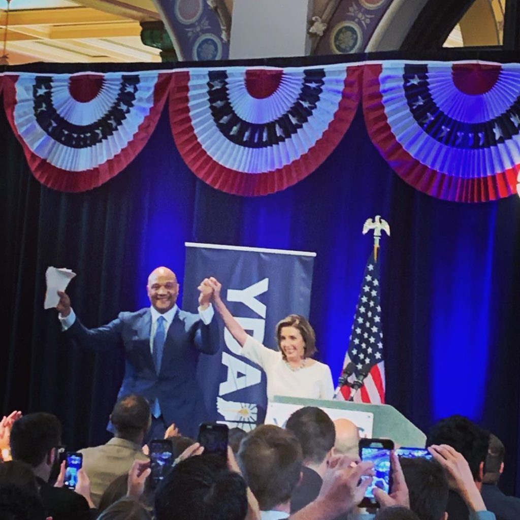Speaker of the House Nancy Pelosi and Congressman Andre Carson holding hands with arms raised at the Young Democrats of America National Convention in Indianapolis 2019